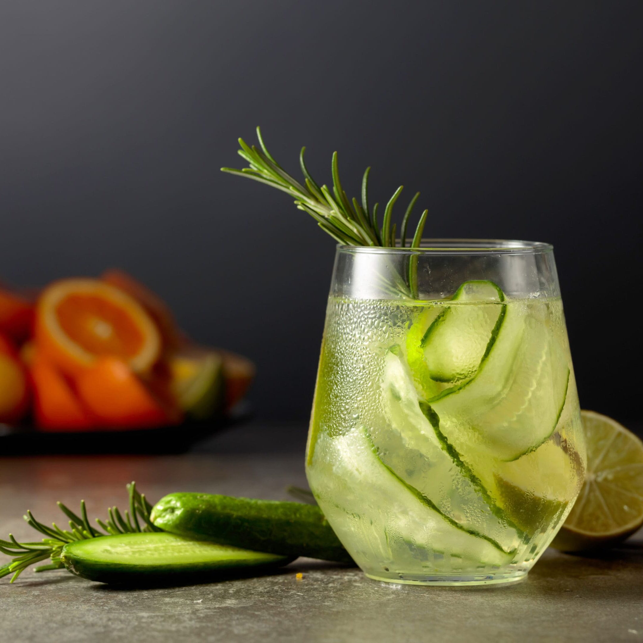 Cocktail gin tonic with ice, rosemary, lime, and cucumber on a stone table. Cocktail, lime, straw, martini glass.